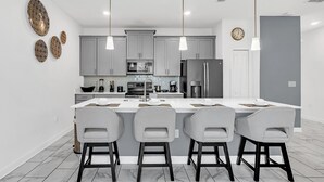 A modern kitchen with a central island, grey cabinets, and pendant lighting.