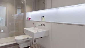 Moderni kylpyhuone, jossa on lasinen suihkuseinä, valkoinen pesuallas ja wc-istuin.