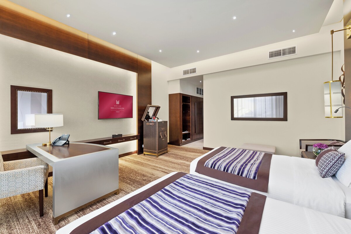 Una habitación de hotel con escritorio, dos camas, un armario y un espejo.