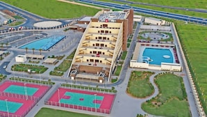 An aerial view of a sports complex with multiple tennis courts, a swimming pool, and a large building with multiple floors. - Grand Millennium Tabuk (Tabuk)