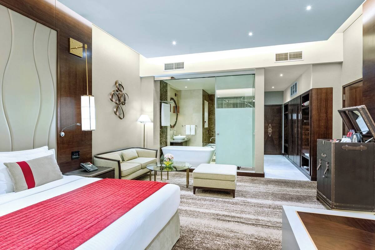A hotel room with a bed, a sitting area, a bathroom, and a wardrobe.