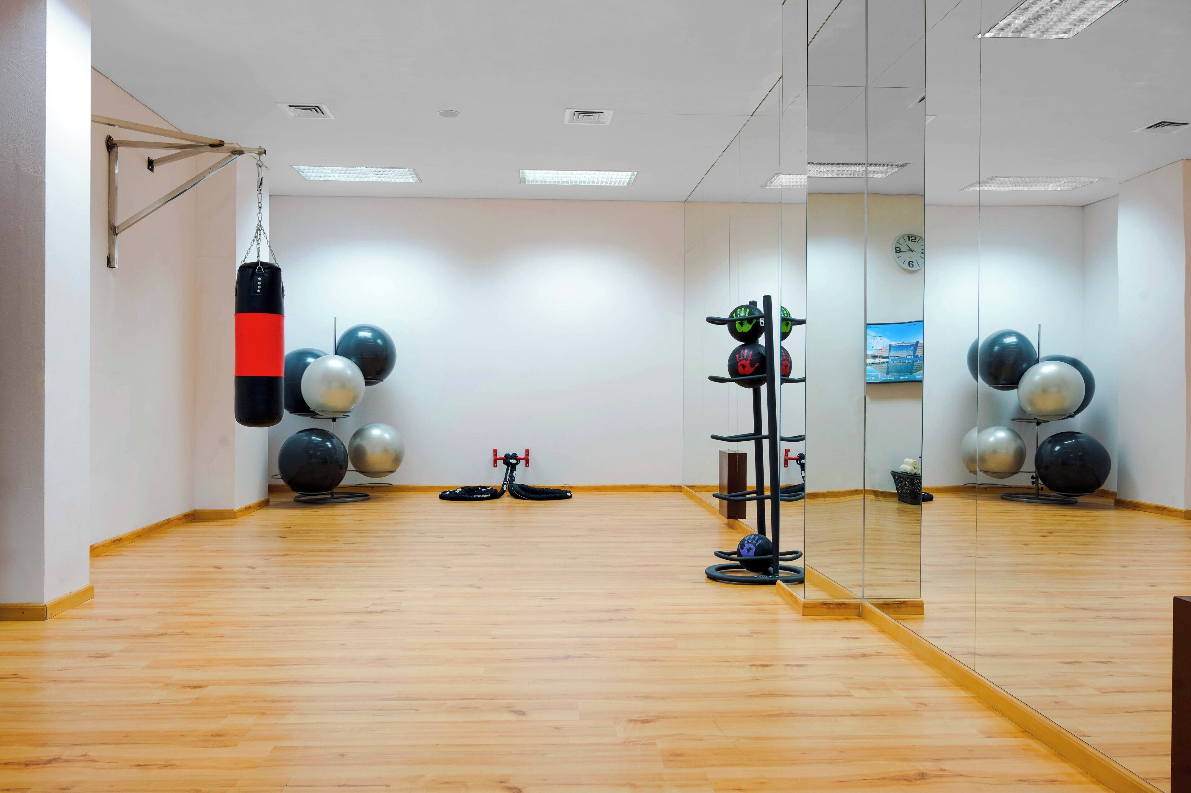 Une salle de sport avec un plancher en bois, des ballons d’exercice, un sac de frappe et un miroir.