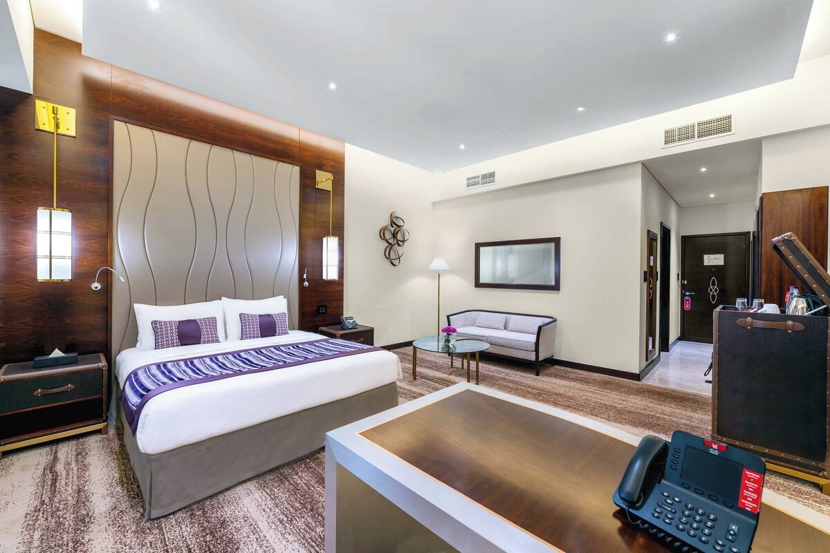 A hotel room with a large bed, a desk with a telephone, a sofa, a small table, and a mirror.