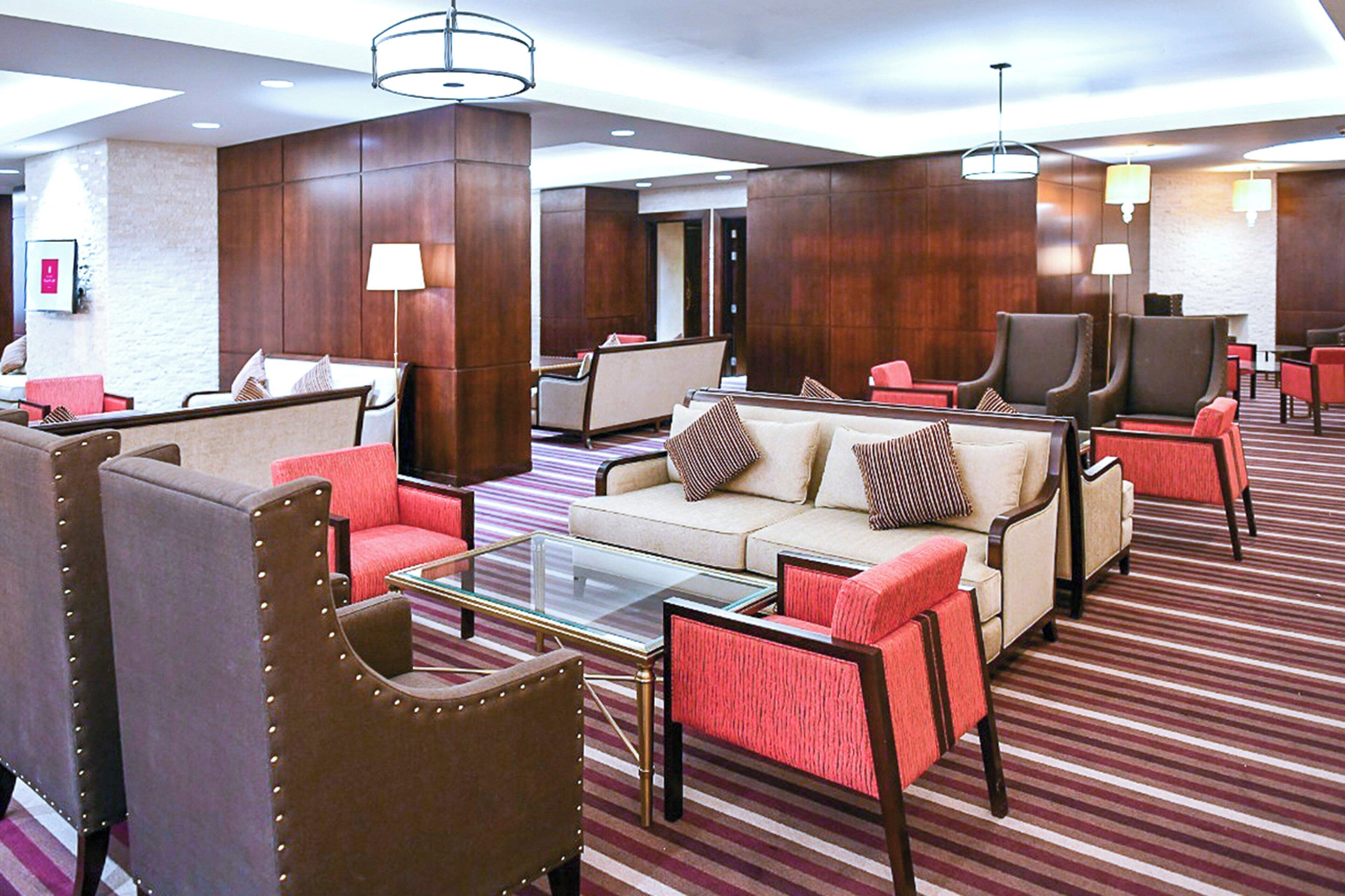 En hotelllobby med ett randigt golv, flera sittgrupper med soffor och fåtöljer samt ett bord i glas.