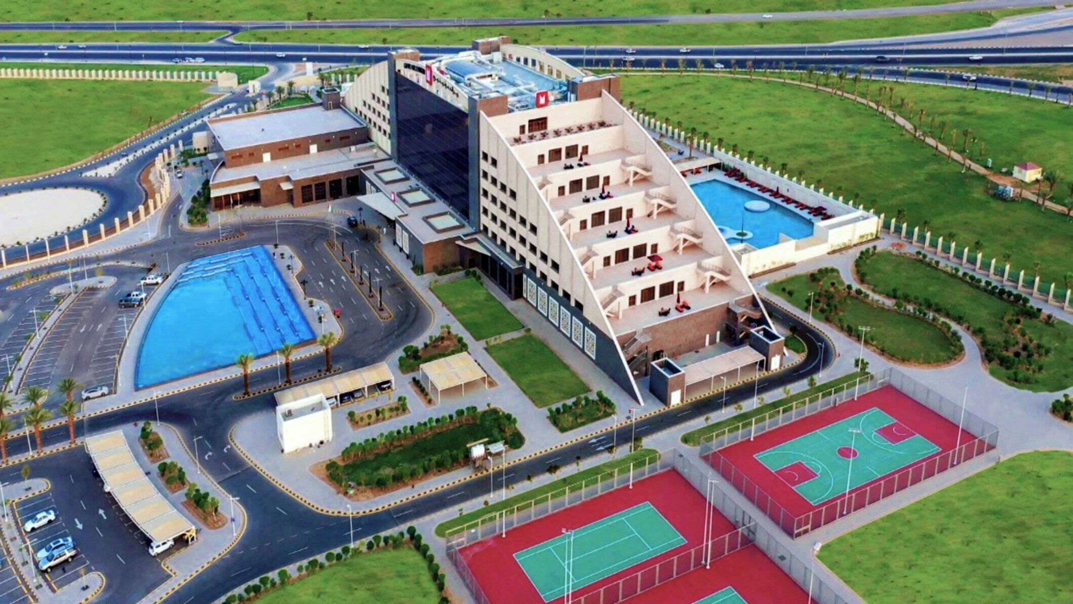 Un edificio moderno con piscina, canchas de tenis y jardines ajardinados.