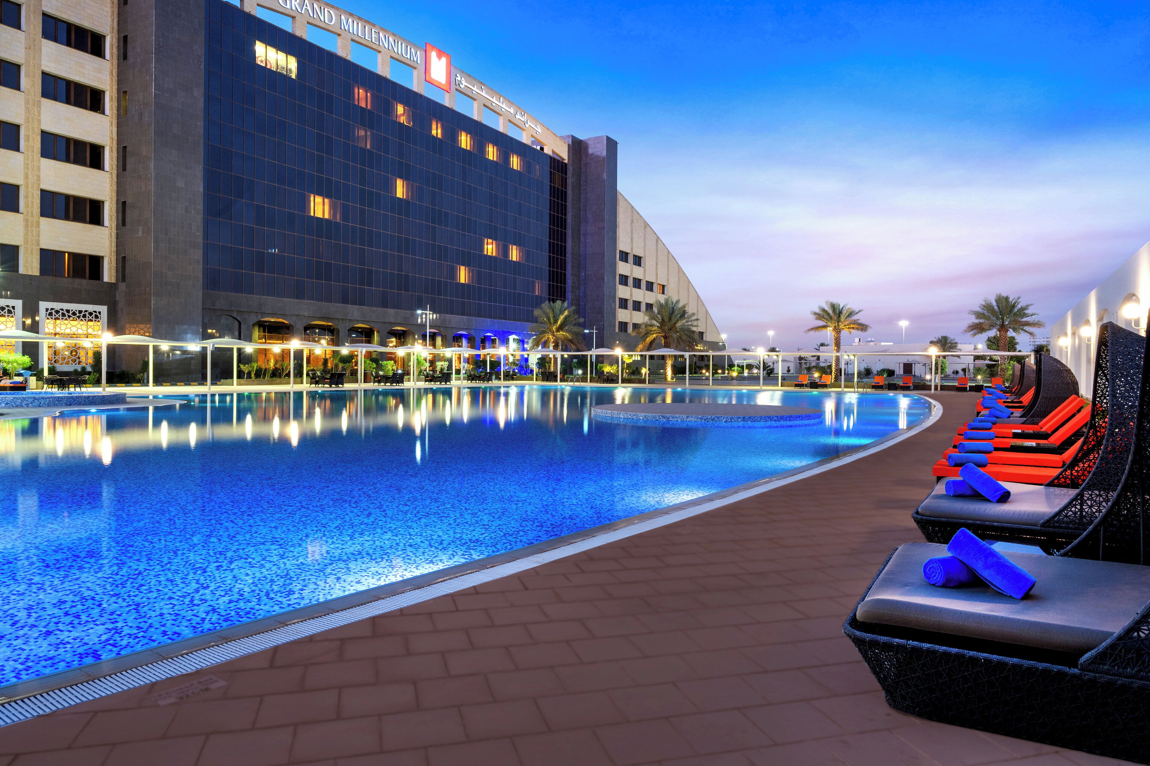 A hotel with a large swimming pool, lounge chairs, and palm trees.