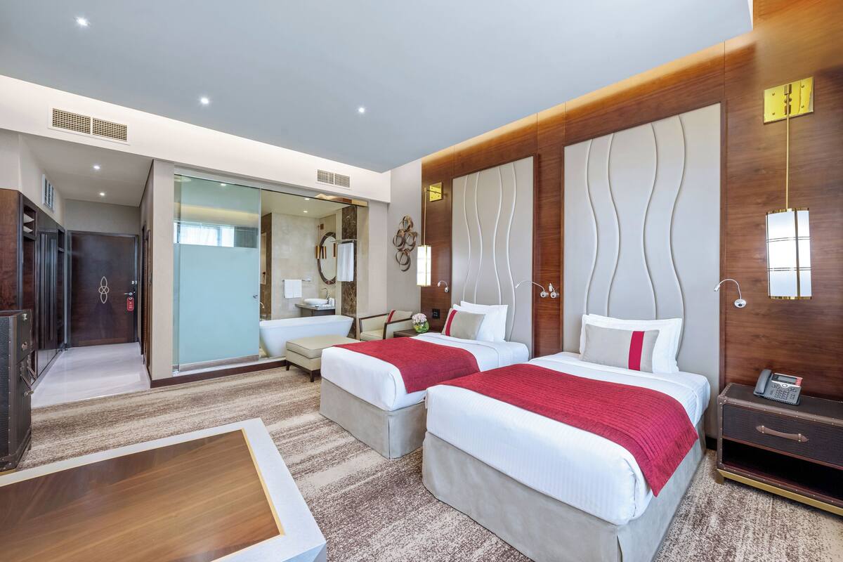 A hotel room with two beds, a desk, a chair, and a wardrobe.