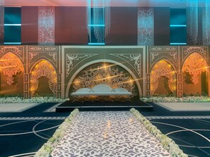 A stage with ornate arches and a central seating area, surrounded by a patterned floor and floral arrangements.