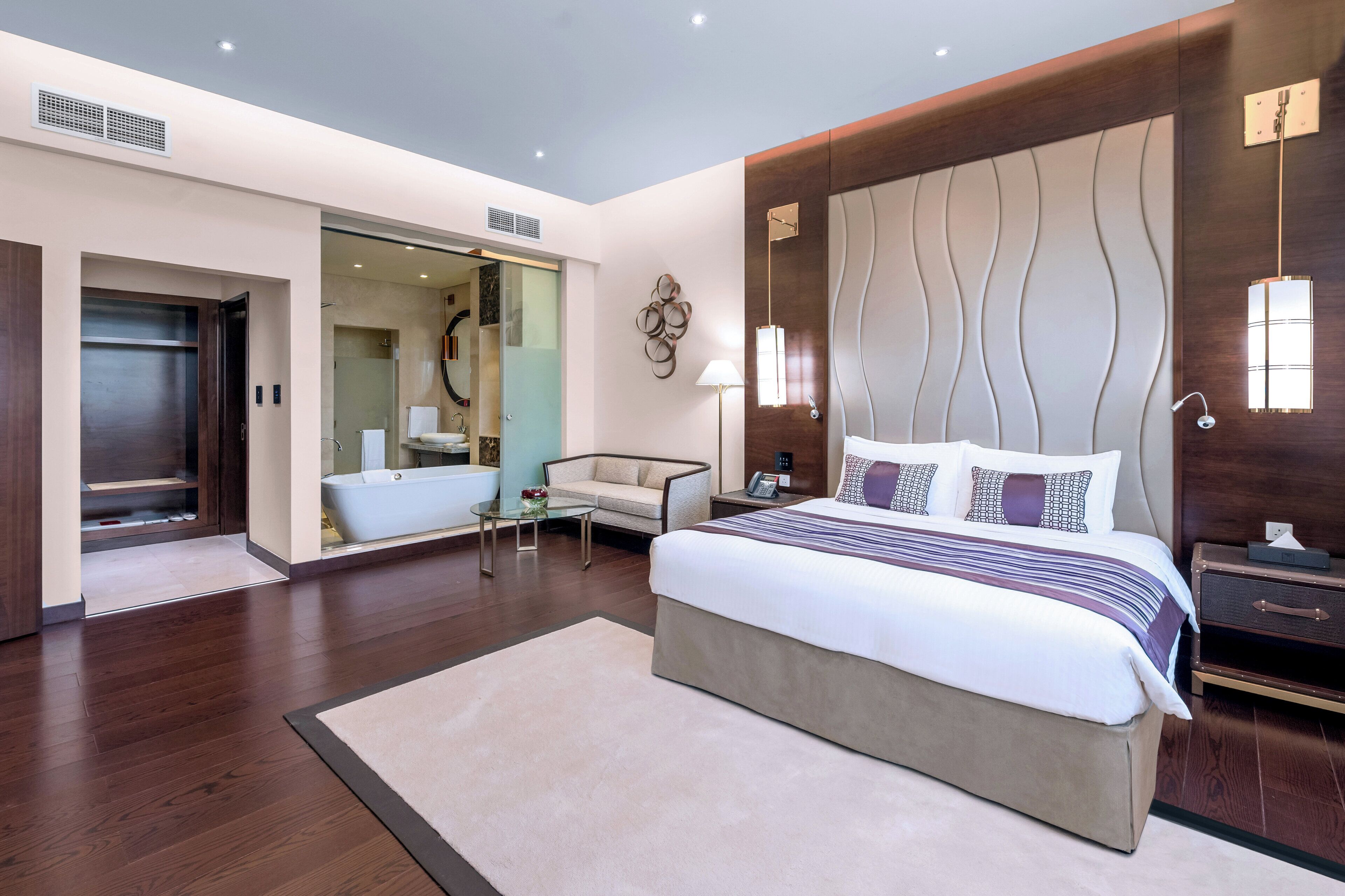 A modern hotel room with a large bed, a sitting area, a bathroom, and a wardrobe.