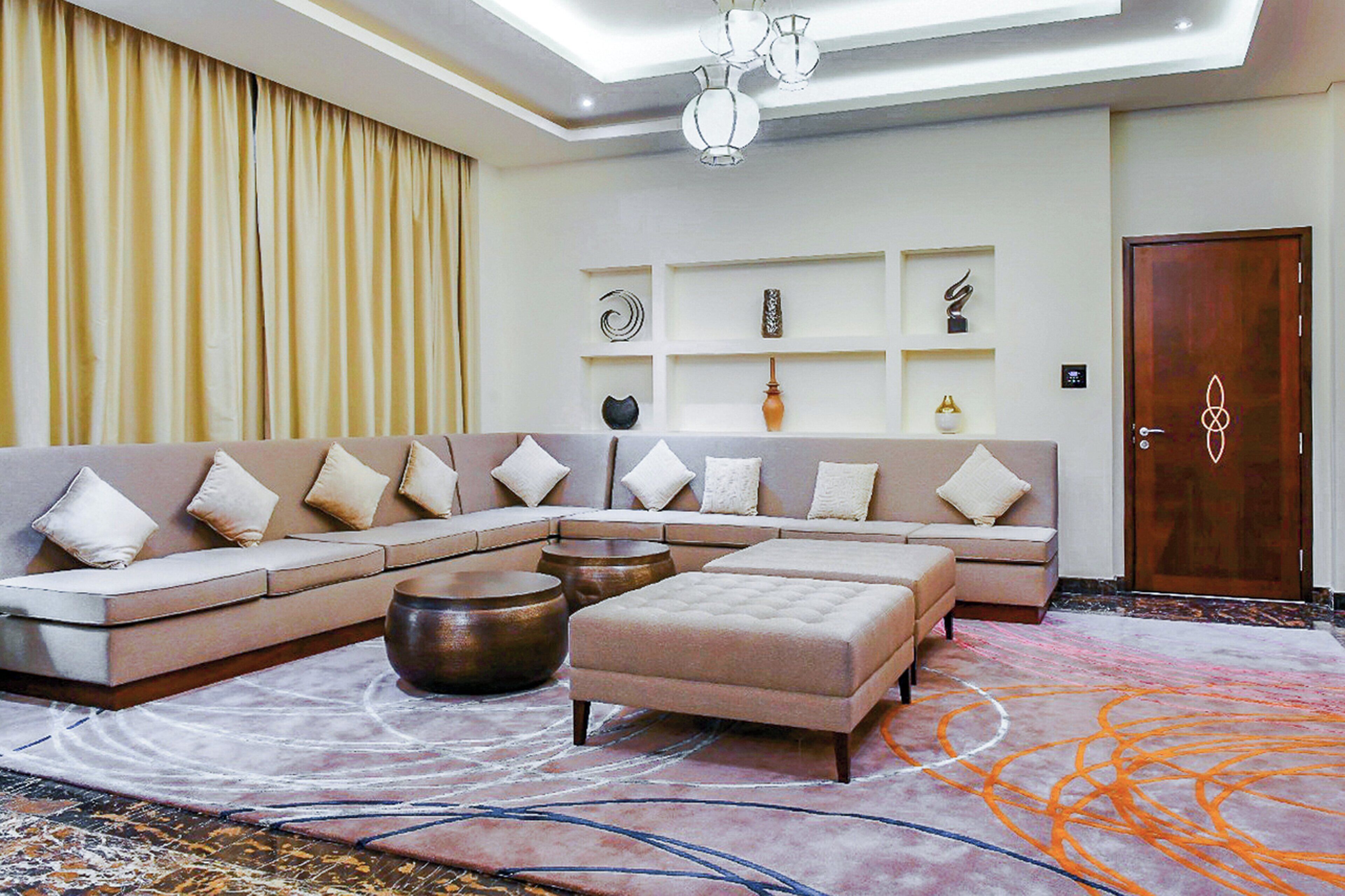 Una sala moderna con un sofá seccional, un reposapiés y objetos decorativos en estantes.