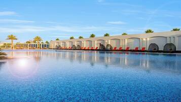 Una piscina con sillones de descanso y palmeras.