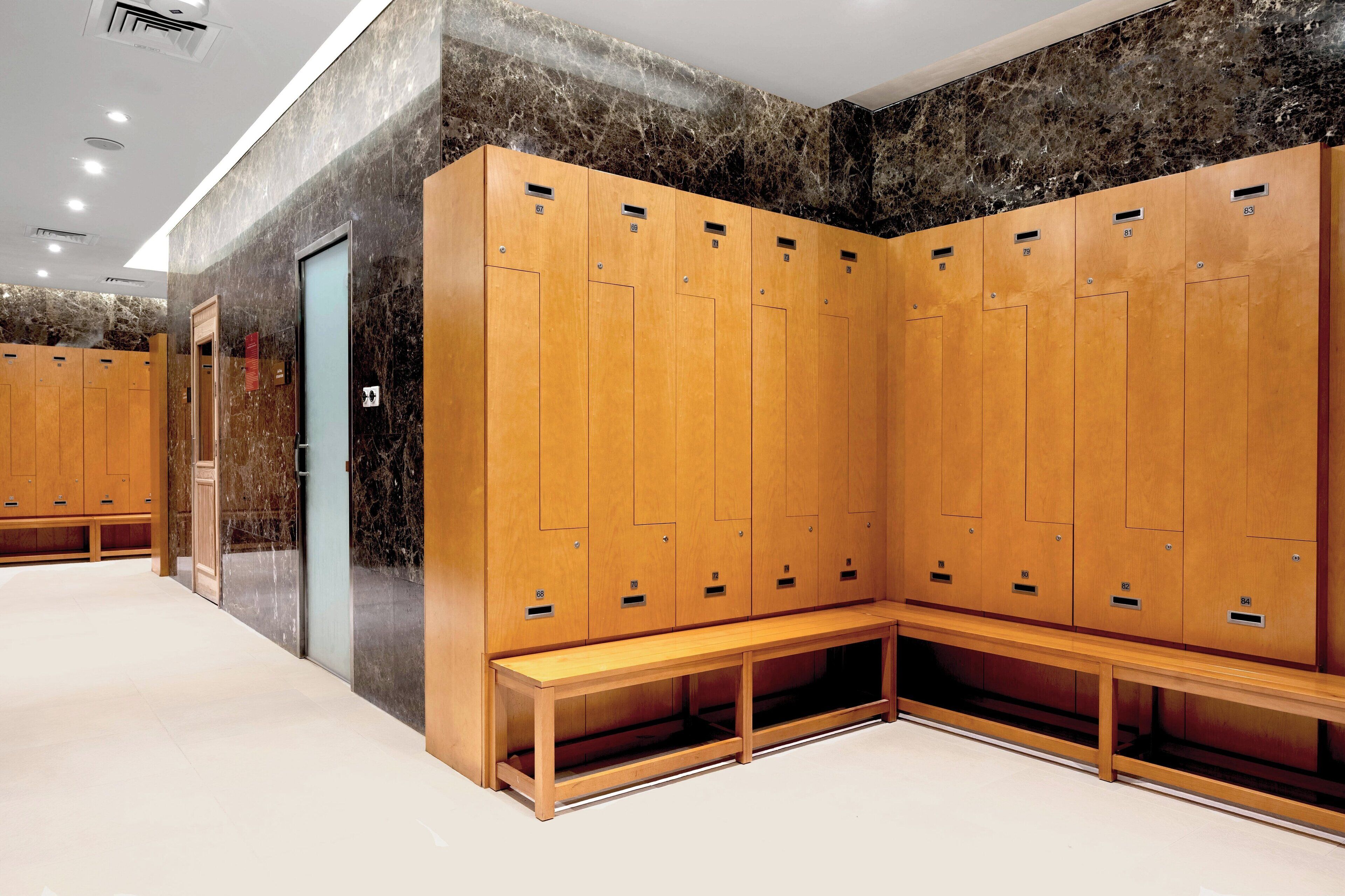 Un vestuario moderno con taquillas de madera, un banco y paredes de mármol.