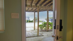Una puerta que da a un espacio exterior con piso de concreto, pilares de madera y vista a una casa y vehículos al fondo.