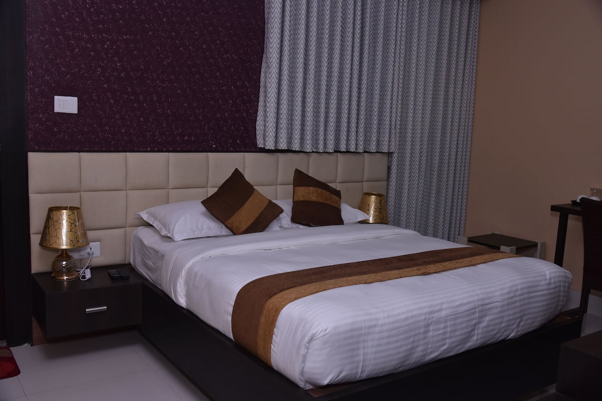 A neatly made bed with a brown throw, a bedside lamp, and a nightstand with a remote control.
