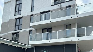 Een modern gebouw met een plat dak, meerdere balkons en een overdekt terras met stoelen en tafels.