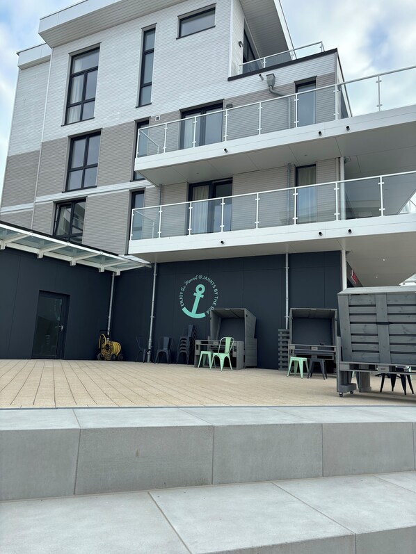 A modern building with a flat roof, multiple balconies, and a covered outdoor seating area with chairs and tables.