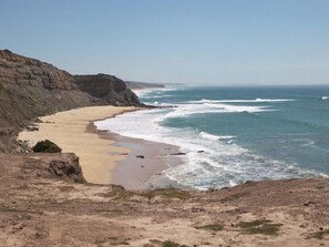 A coastal landscape with a sandy beach, rocky cliffs, and the ocean.