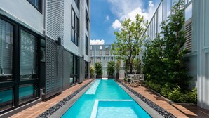 Ein moderner Poolbereich mit einem klaren, blauen Pool, umgeben von einer gefliesten Terrasse und einer Reihe von Gebäuden mit großen Fenstern und einer geometrischen Fassade.