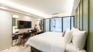 Ein modernes Hotelzimmer mit einem großen Bett, einem Schreibtisch, einem Flachbildfernseher, einem Sessel und einem großen Fenster.