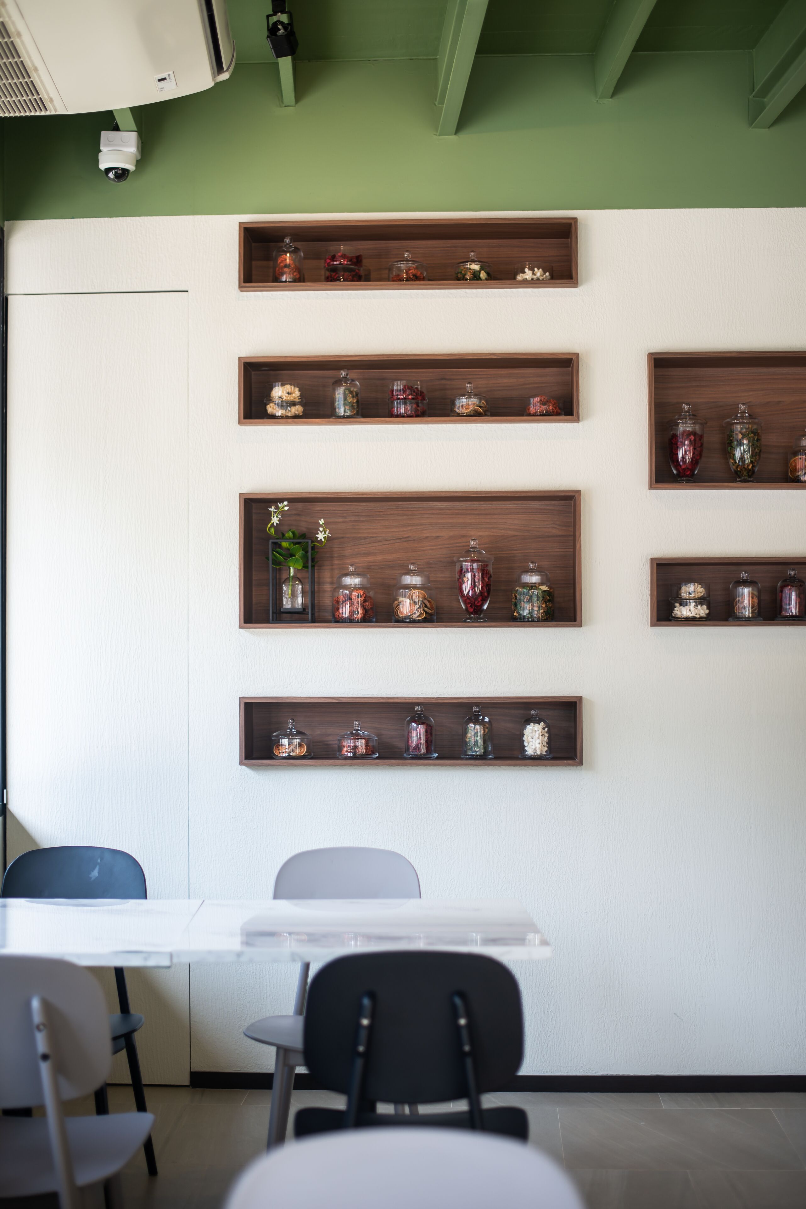A room with a white table, four wooden shelves with jars, and a green wall.