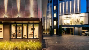 A modern hotel entrance with a glass facade, a brick pathway, and a well-lit reception area.