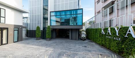 Un edificio moderno con fachada de vidrio, un letrero que dice "KAYA HERITAGE" y un camino de entrada empedrado.