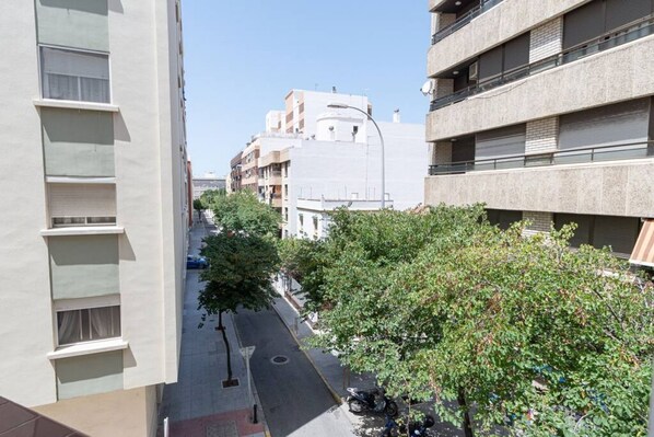 A narrow urban street lined with multi-story buildings, trees, and parked motorcycles.