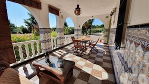 Eine überdachte Terrasse mit Fliesenboden, einem Tisch mit Stühlen und einem hängenden Laternen.