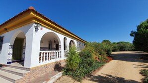 Ein weißes Gebäude mit gelbem Dach und mehreren Bögen, umgeben von Grünpflanzen und blauem Himmel.