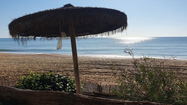 Ein Strand mit einem strohgedeckten Sonnenschirm und Blick auf das Meer.