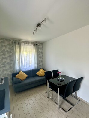 A modern living room with a grey sofa, two yellow cushions, a dining table with four chairs, and a ceiling light fixture. - Residence Beni 6 with large heated pool (Medulin, Pula)