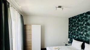 Une chambre d’hôtel avec deux lits, une armoire en bois, une tête de lit à motifs géométriques et un luminaire au plafond.