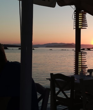 Une vue sur la mer depuis un restaurant, avec une table et des chaises, donnant sur des eaux calmes et des montagnes lointaines.