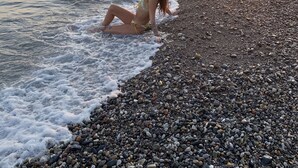 Une plage de galets où une personne est assise au bord de l’eau, au coucher du soleil.