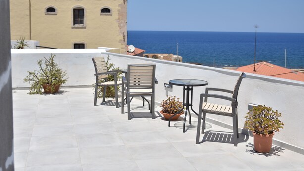 Une terrasse sur le toit, avec une table et des chaises, des plantes en pot et une vue sur la mer.