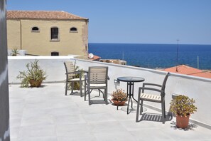 A rooftop terrace with a table and chairs, potted plants, and a view of the sea. - Porto Chania (Chania)