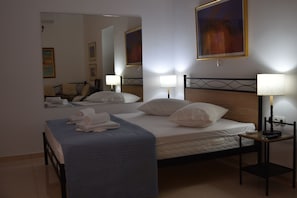 Un lit bien fait, recouvert d’une couverture bleue, avec deux lampes de chevet et un grand miroir au-dessus du lit.