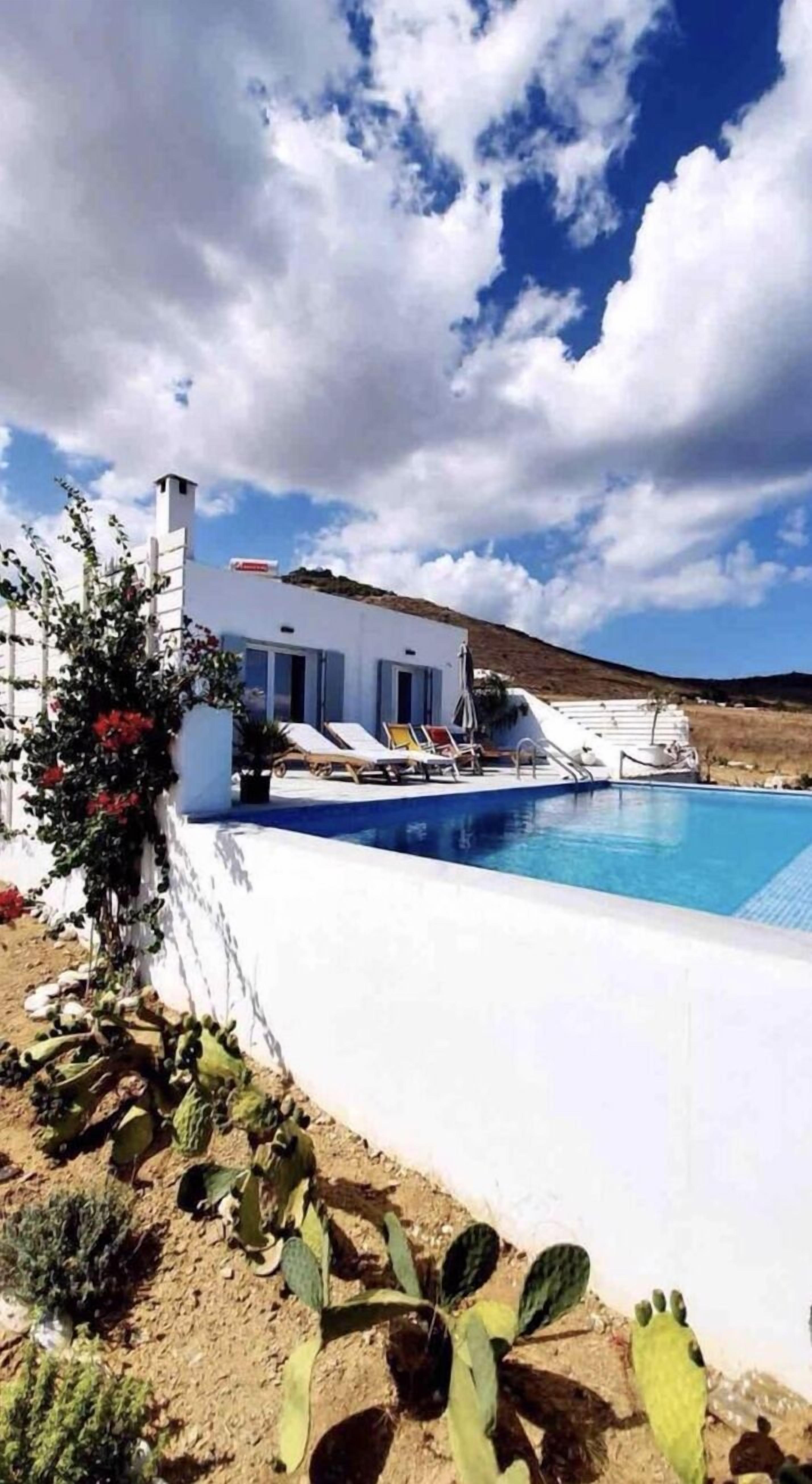 Eine moderne weiße Villa mit Pool, umgeben von Kakteen und wolkenlosem, blauem Himmel.