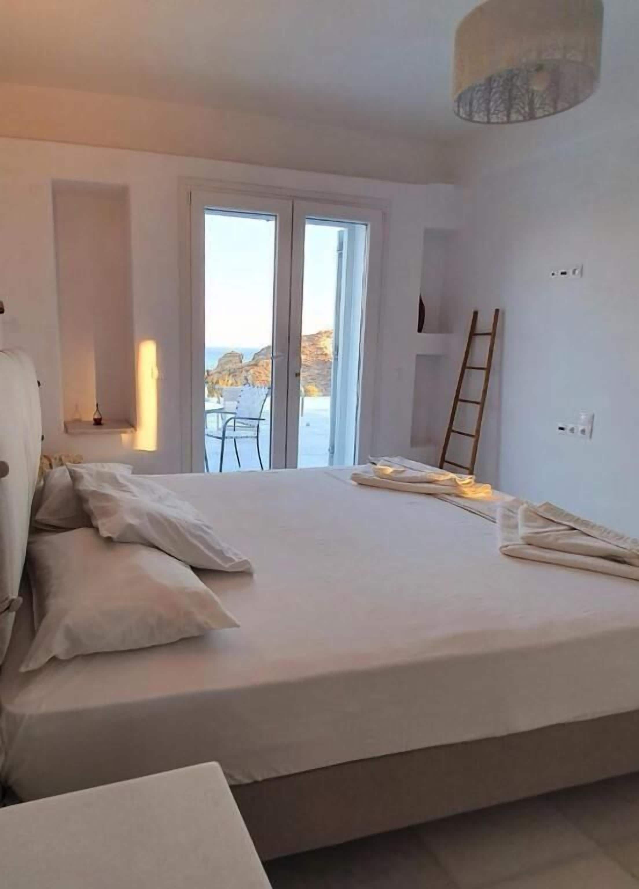 A bedroom with a large bed, a balcony with a view, and a ladder against the wall.
