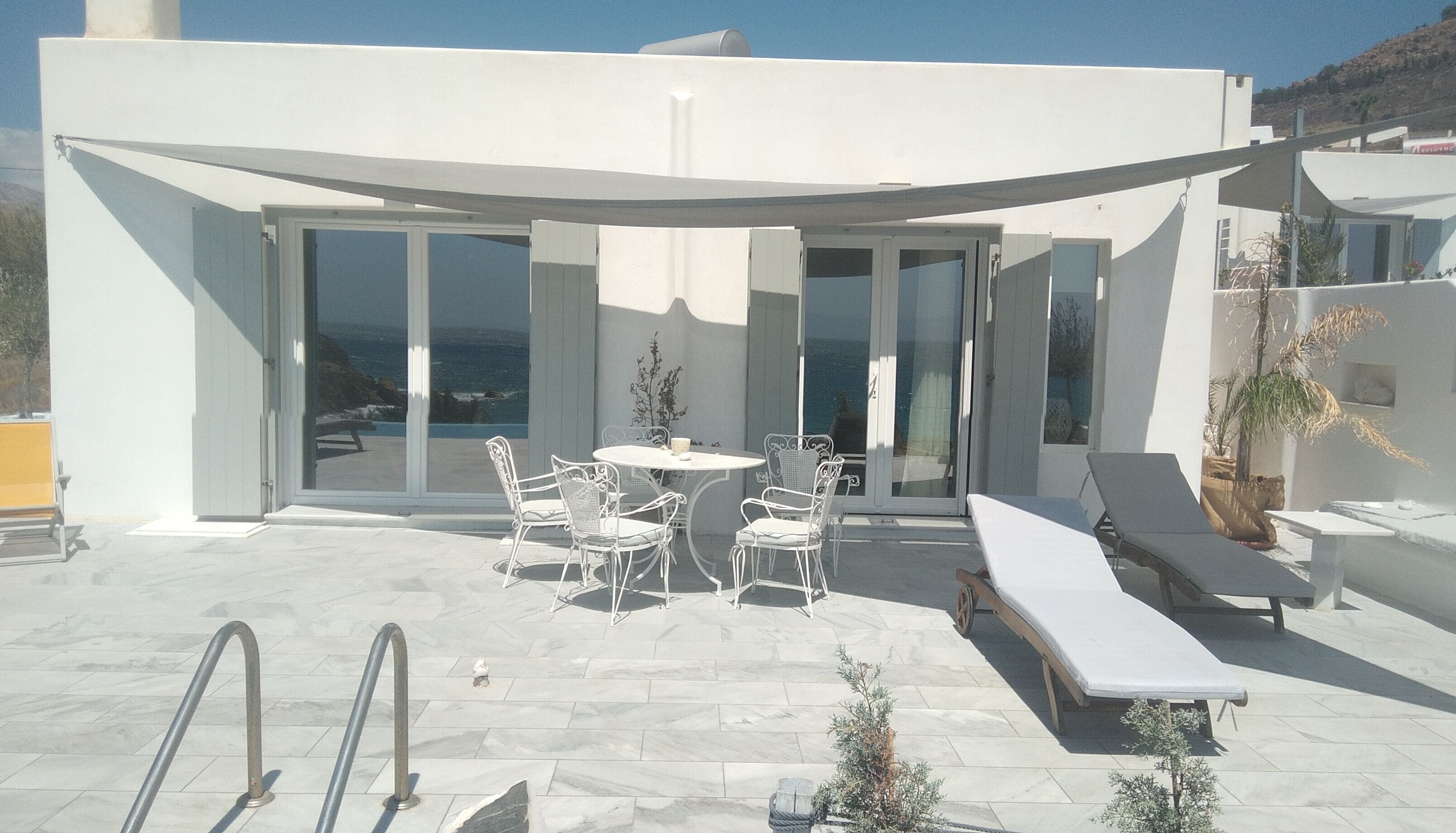 Un patio exterior moderno con piscina, mobiliario blanco y vista al mar.