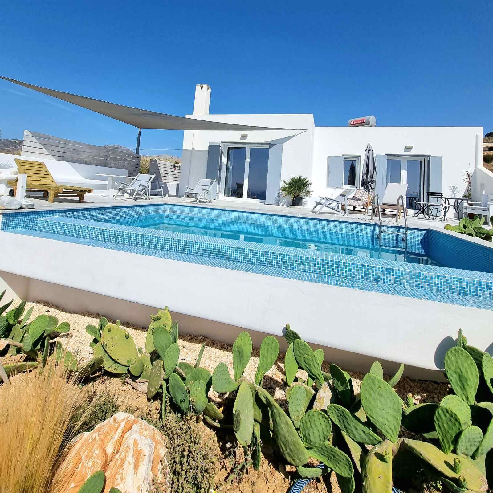 A modern pool area with a clear blue pool, surrounded by white walls and a white building with a flat roof.
