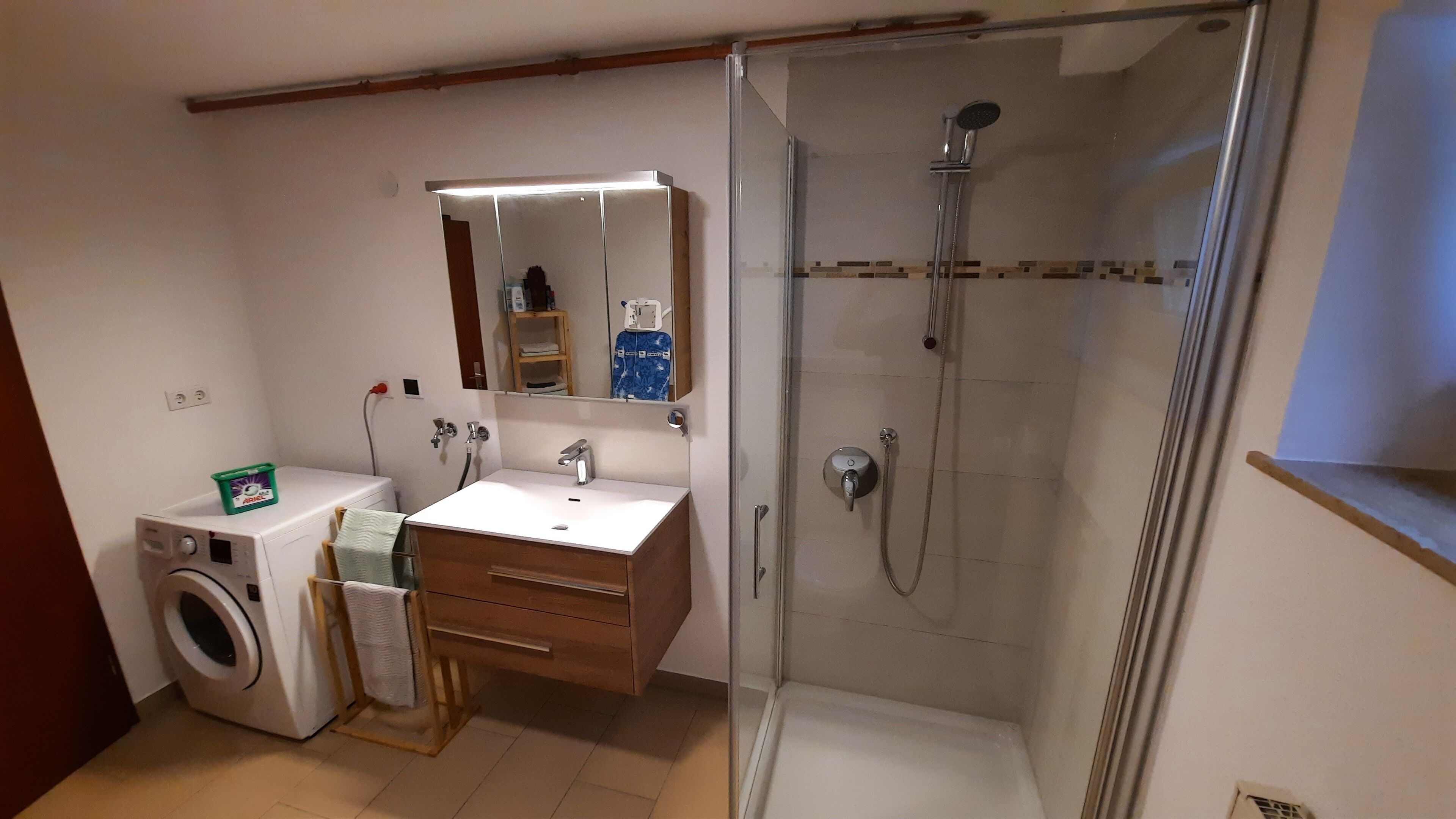 A compact bathroom with a washing machine, a sink, a mirror, and a shower.
