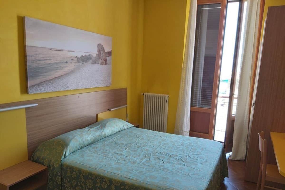 A room with a bed, a wooden headboard, a radiator, and a window with curtains.