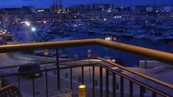 Un balcone con un tavolo, su cui si trovano una bottiglia e dei bicchieri, con vista su una marina piena di barche ed edifici.