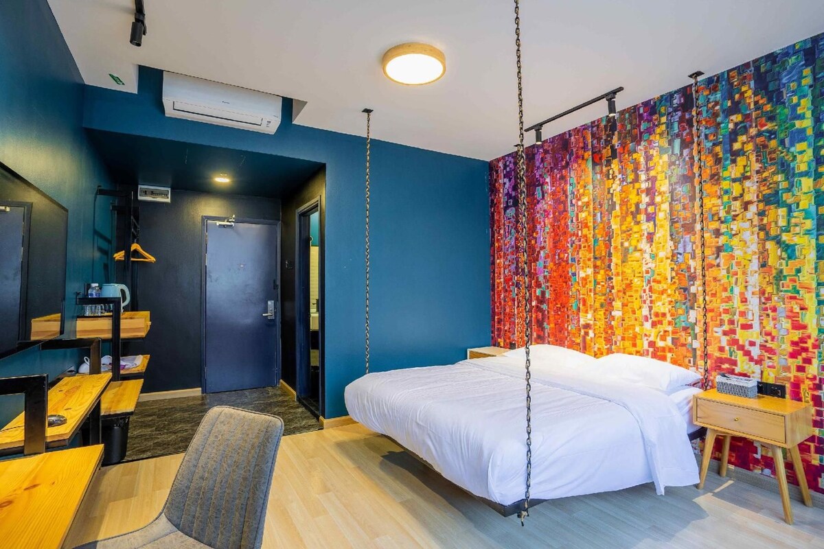 Une chambre d’hôtel moderne équipée d’un lit, d’un bureau, d’une chaise et d’un mur décoré d’une mosaïque aux couleurs vives.