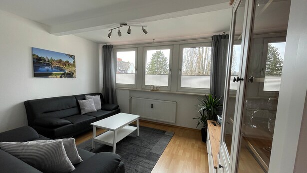 Una sala moderna con un sofá negro, una mesa de centro blanca y vistas al exterior a través de amplios ventanales.