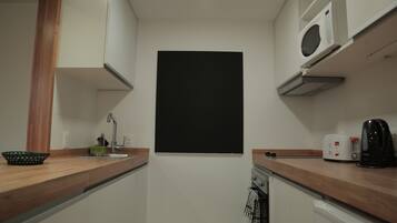 A compact kitchen with white cabinets, a wooden countertop, a blackboard, a microwave, a toaster, and a kettle.