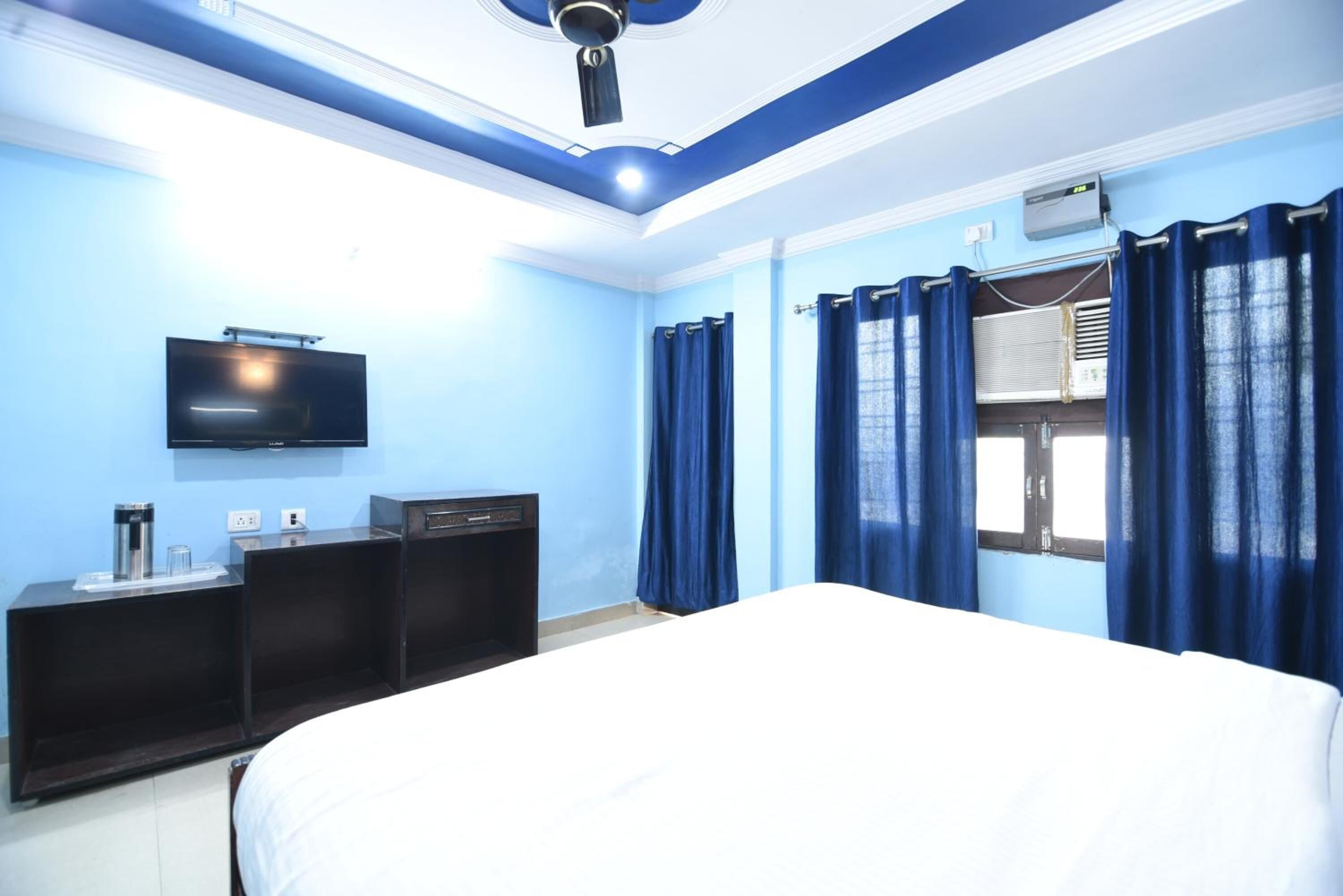 A hotel room with a bed, a TV mounted on the wall, a desk with a coffee maker, and a window with curtains.