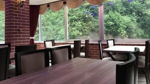 A restaurant with a brick fireplace, large windows with curtains, and a wooden table and chairs. - Vulada Butik Otel (Ardesen)