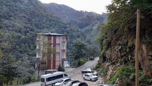 A multi-story building with balconies, a parking area with several cars, and a mountainous backdrop. - Vulada Butik Otel (Ardesen)
